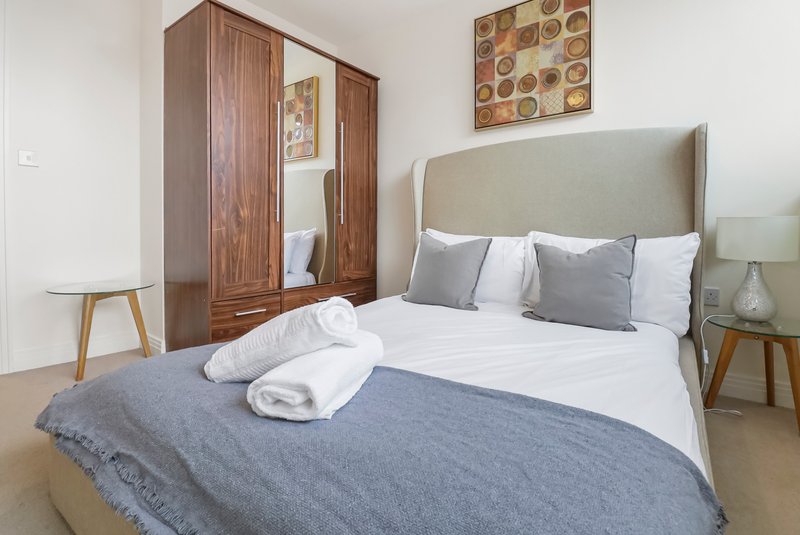 Bright bedroom with upholstered bed, wooden wardrobe, side tables and wall art