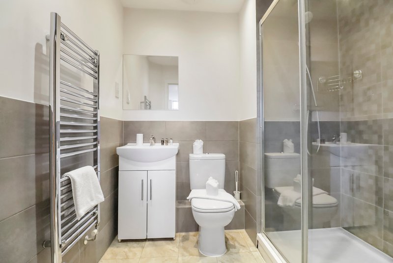 Modern bathroom with white sink vanity, toilet, heated towel rail and shower enclosure