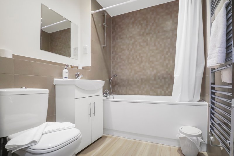 Modern bathroom with toilet, sink vanity, mirror, bathtub with shower curtain and heated towel rail