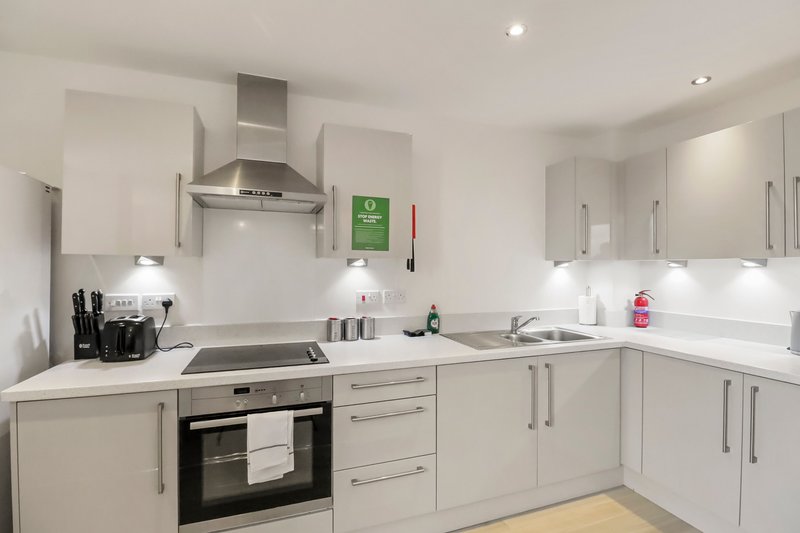 Modern white kitchen with built-in oven, induction hob, and stainless steel range hood