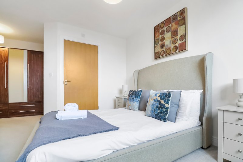 Modern bedroom with double bed, upholstered headboard, blue throw and decorative pillows