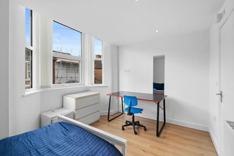 Bright bedroom with single bed, desk, blue office chair and large windows