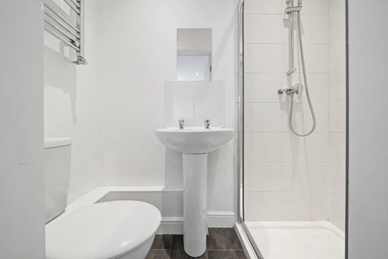 Clean modern bathroom with white toilet, pedestal sink, shower cubicle and towel rail