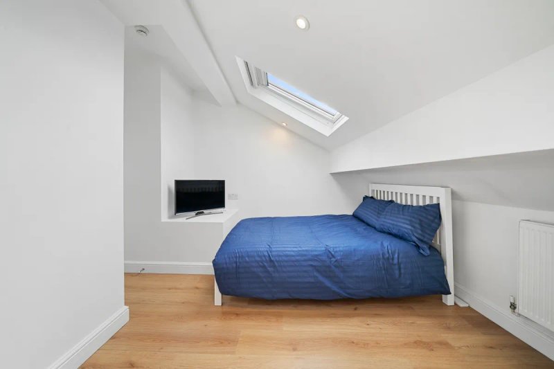 Attic bedroom with blue bedding, wooden floor, skylight window and small TV