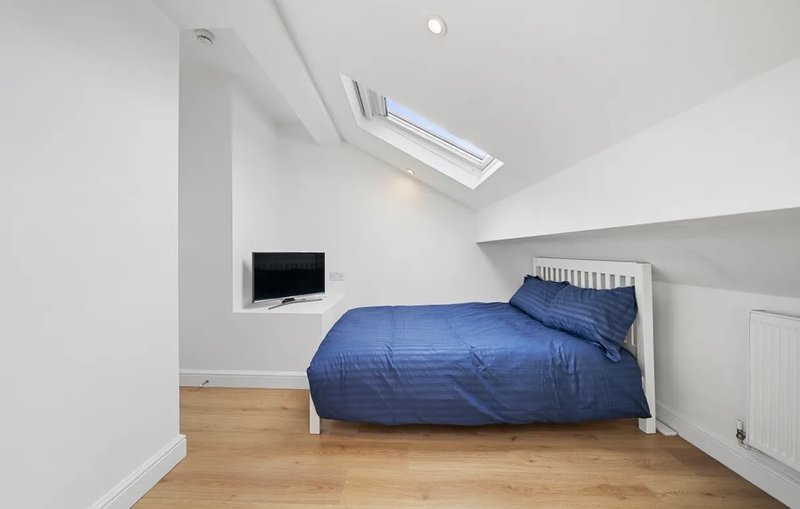 Attic bedroom with blue bedding, skylight window, wooden flooring and small TV