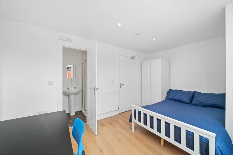 Bright bedroom with single bed, blue bedding, wooden floor and ensuite bathroom door