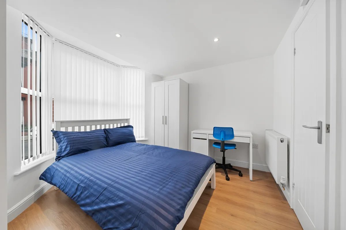 Bright bedroom with blue striped bedding, desk chair, wardrobe and wooden flooring