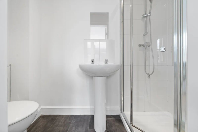 Clean modern bathroom with pedestal sink, toilet, shower enclosure and window
