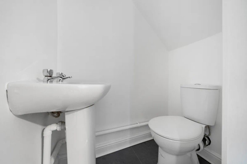 Small bathroom with pedestal sink, toilet, white walls and dark floor