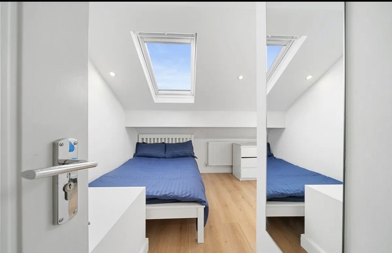 Bright attic bedroom with two single beds, blue bedding, skylight windows and wooden flooring