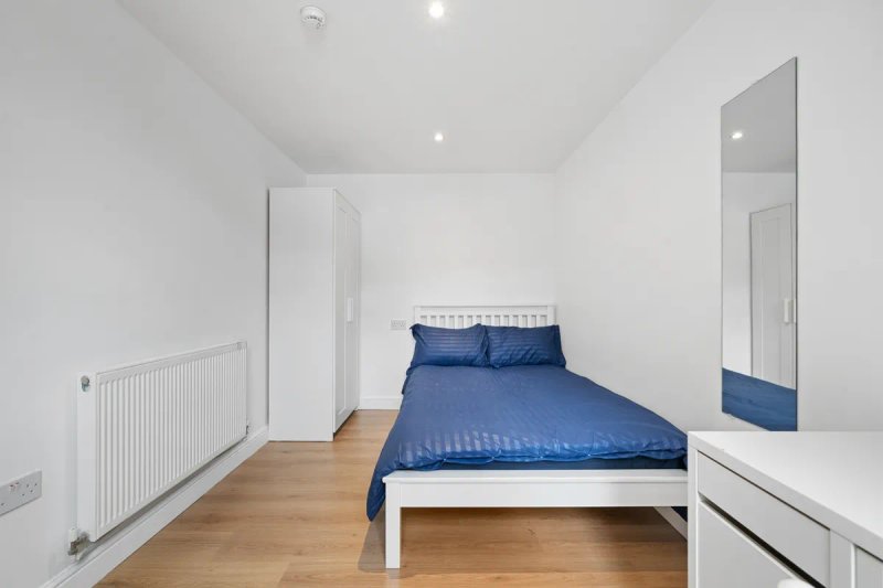 Modern bedroom with white bed frame, blue bedding, wooden floor and mirror