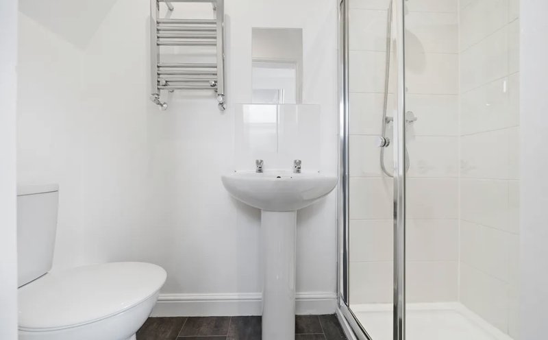 Clean bathroom with white walls, pedestal sink, toilet, heated towel rail and shower cubicle