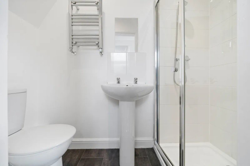 Clean modern bathroom with toilet, pedestal sink, towel rail and shower enclosure