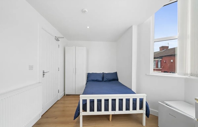 Bright bedroom with single bed, wooden floor, window with street view, and white walls
