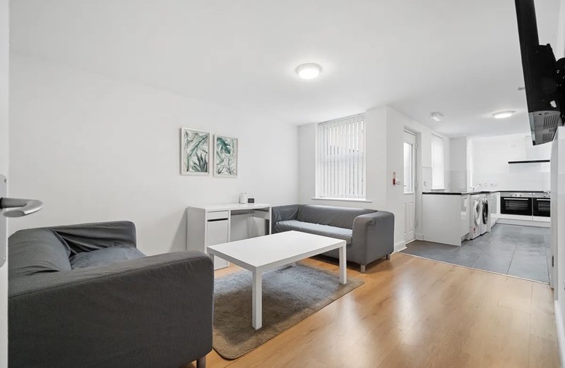 Open-plan living room and kitchen with grey sofas, white coffee table, and modern appliances