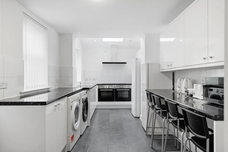 Modern galley kitchen with white units, black countertops, integrated appliances and breakfast bar seating