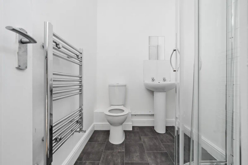 Modern bathroom with toilet, pedestal sink, heated towel rail and dark tile flooring