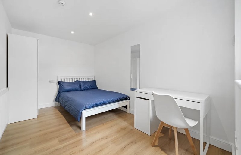Bright bedroom with blue double bed, wooden floor, desk, chair and wardrobe
