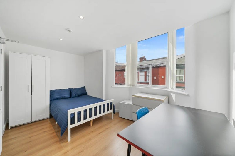Bright bedroom with single bed, wardrobe, desk, wooden floor and street-facing windows