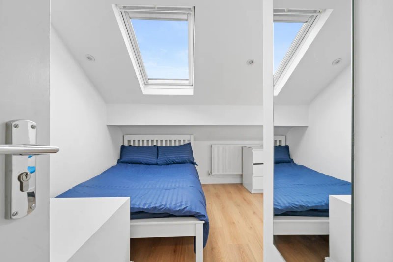 Bright attic bedroom with two single beds, blue bedding, skylight windows and wooden flooring