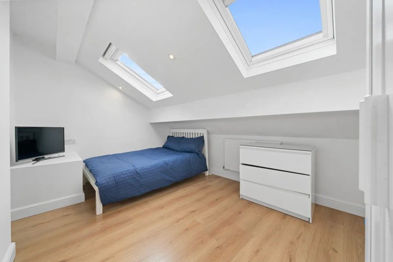 Attic bedroom with single bed, wooden floor, skylight windows and white storage drawers