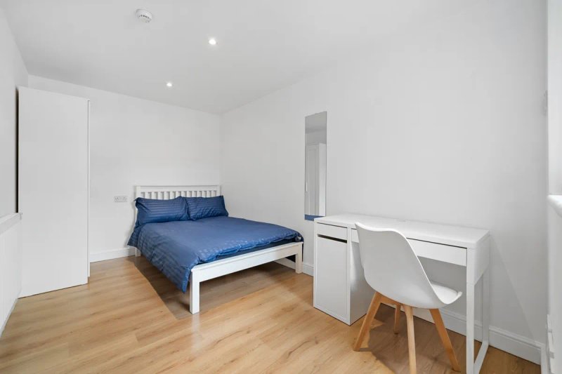 Bright bedroom with double bed, white desk, chair, wooden floor and white walls