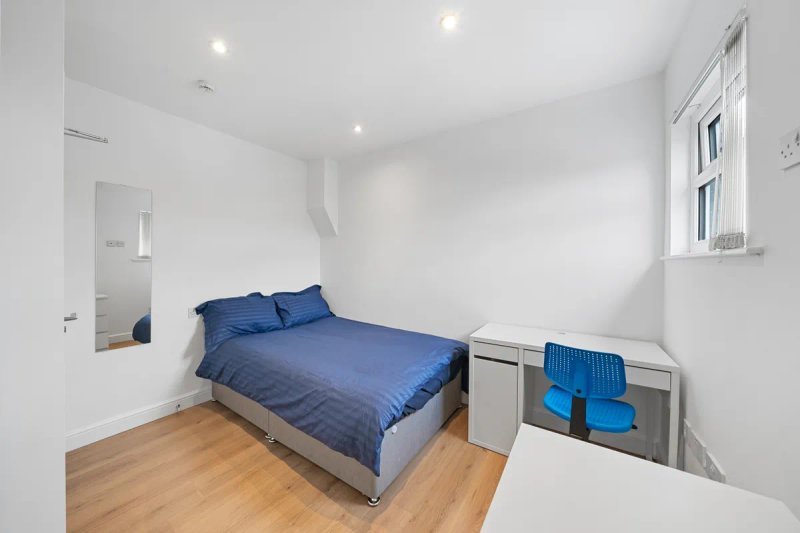 Bright bedroom with double bed, blue bedding, wooden floor and white walls