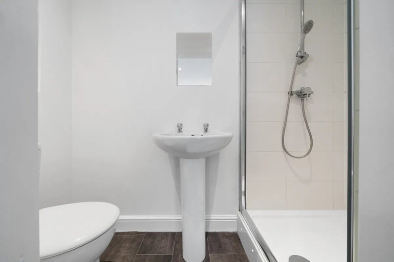 Clean bathroom with pedestal sink, toilet, shower enclosure and small mirror