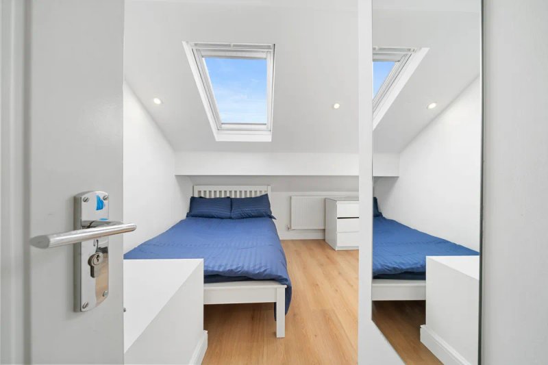 Bright attic bedroom with two single beds, blue bedding, skylight windows and wooden floor