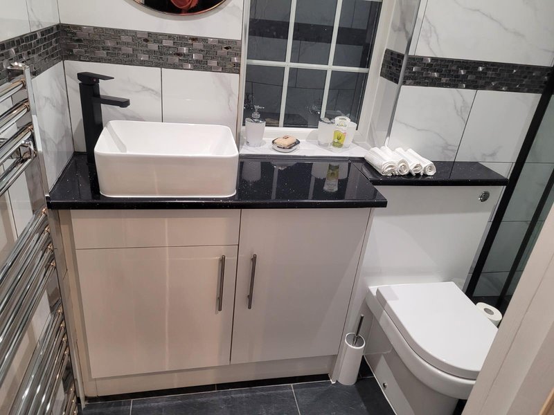 Modern bathroom with white vessel sink, black countertop, toilet, and shower enclosure