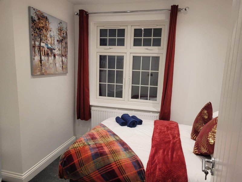 Small bedroom with single bed, plaid blanket, burgundy curtains and framed wall art