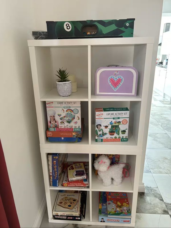 White shelving unit displaying board games, books, decorative items, and a small potted plant
