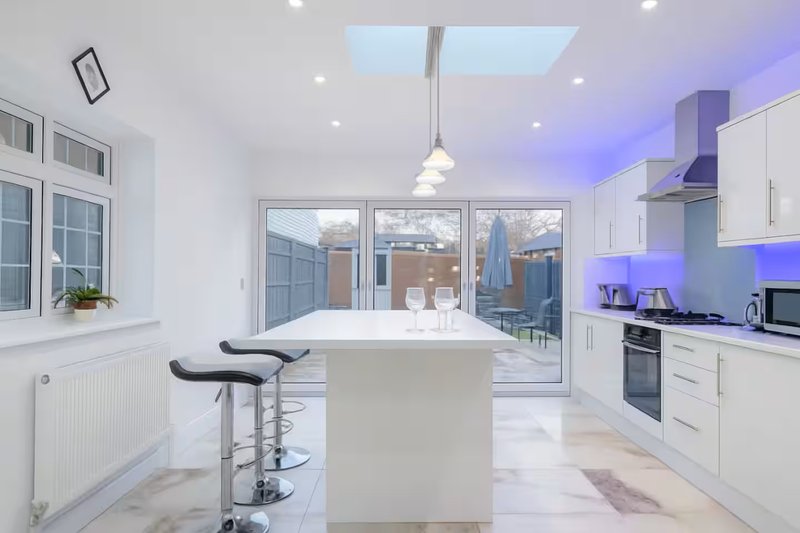 Modern open-plan kitchen with white cabinetry, island seating, and skylights overlooking garden