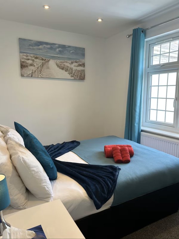 Bright bedroom with double bed, blue pillows, red cushion, and window with blue curtains