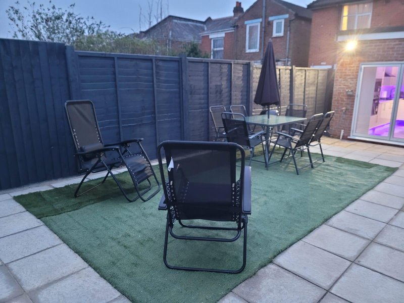 Patio garden with seating area, artificial turf, fence and adjacent brick house