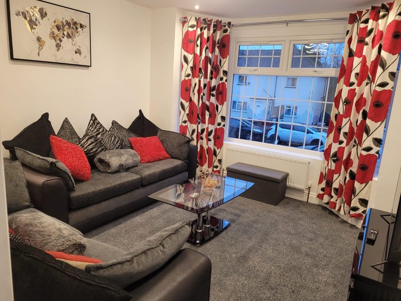 Living room with black and grey sofas, red patterned curtains, cushions, and wall map