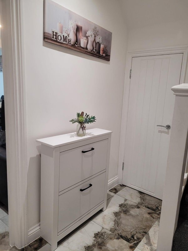Bright entryway with white shoe cabinet, potted plant, and decorative wall art