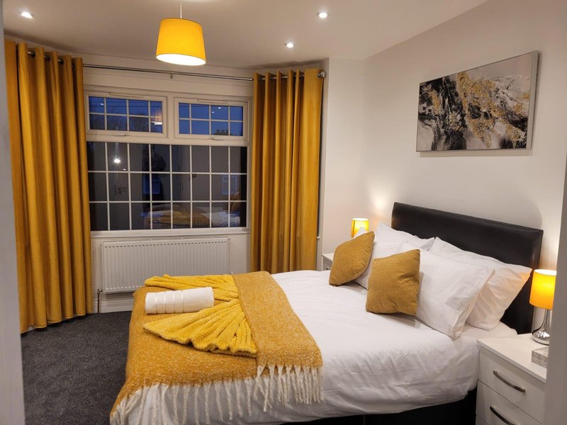 Modern bedroom with double bed, yellow bedding and cushions, pendant light and large window