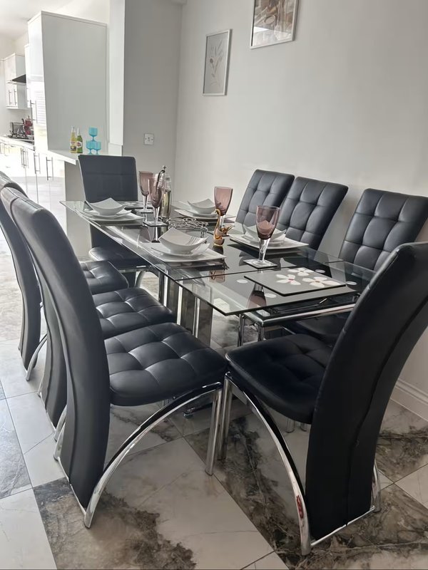 Modern dining area with glass table, black padded chairs, and desktop workspace