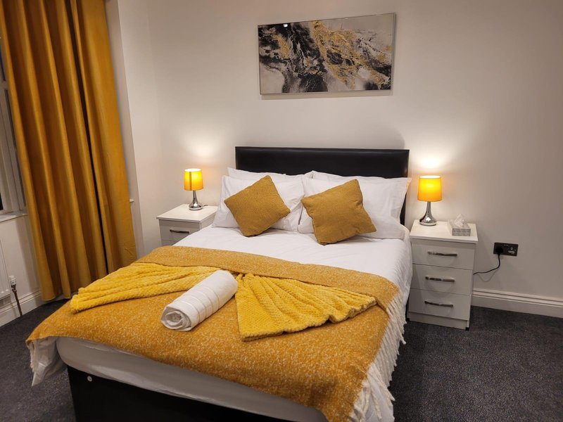 Modern bedroom with double bed, yellow bedding, black headboard, and gold curtains