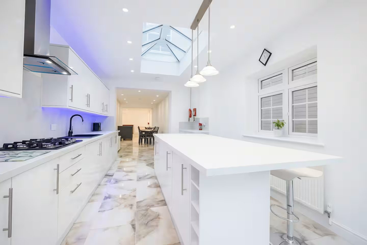 Modern white kitchen with island, gas hob, skylight and open-plan layout to dining area
