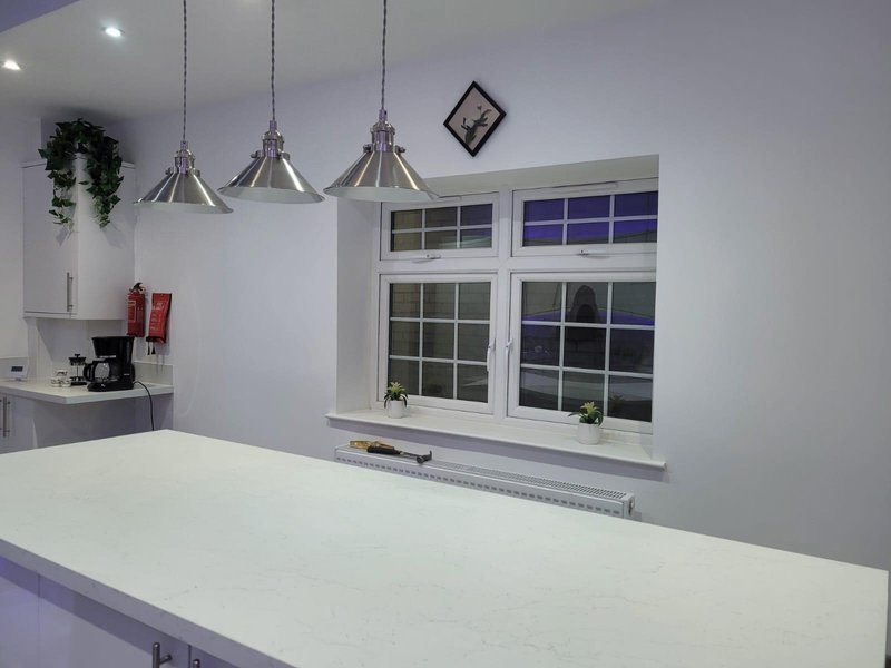 Modern kitchen with white island, pendant lights, and large window overlooking garden