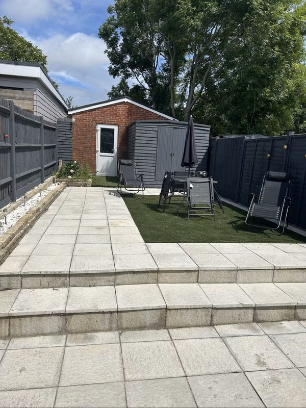 Paved garden area with brick building, loungers and trees in background