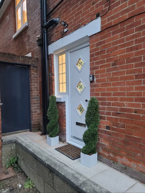 Brick building exterior with light blue door, diamond window panes, and potted topiary plants