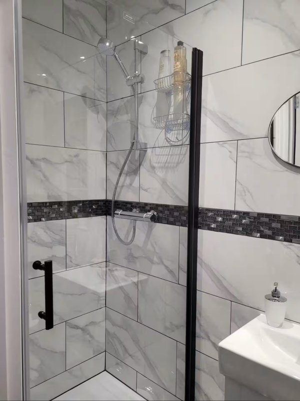 Modern bathroom with marble-tiled shower enclosure, black fixtures, and white sink
