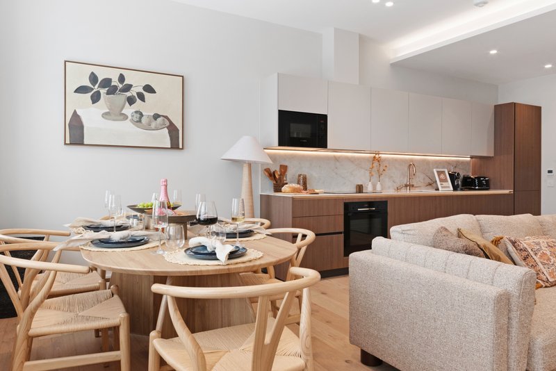 Open-plan kitchen and dining area with wooden table, chairs, cream sofa and modern cabinetry