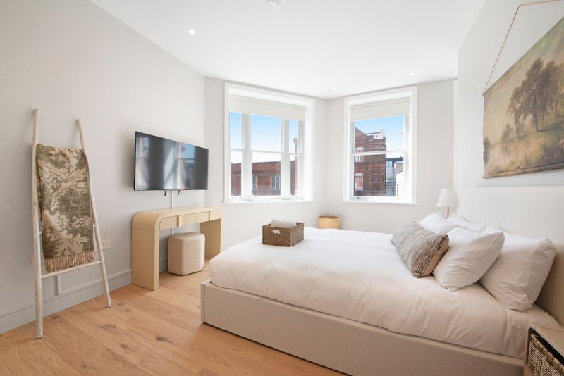 Bright modern bedroom with double bed, wall-mounted TV, wooden floor and large windows
