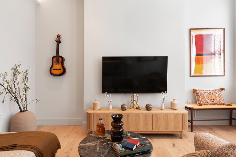 Minimalist living room with wooden TV stand, wall-mounted guitar, framed abstract art, and decorative accessories