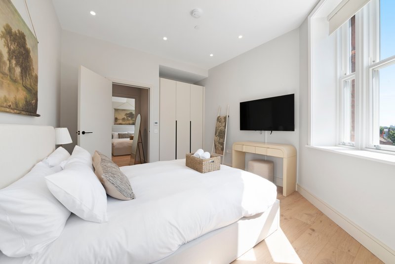 Modern bedroom with double bed, white bedding, wall-mounted TV, wooden flooring and bright windows