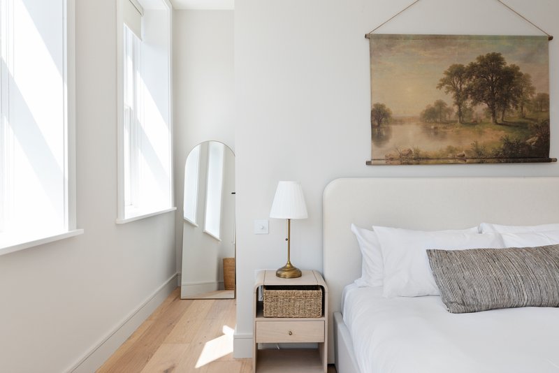 Bright bedroom with double bed, white bedding, wooden nightstand, and large window